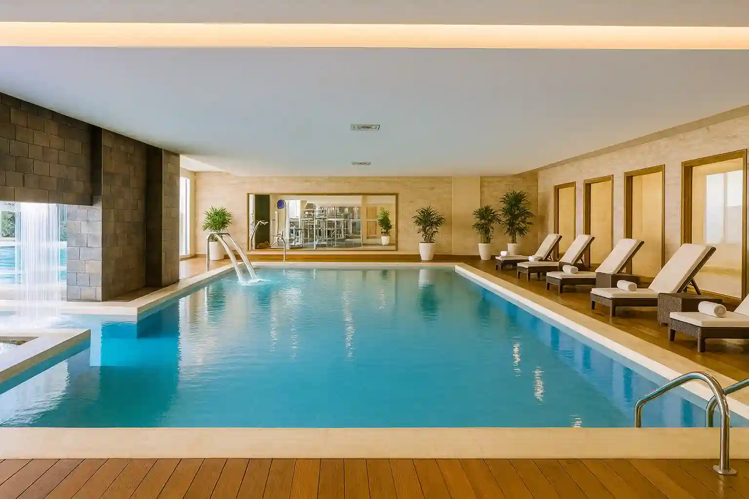 Piscina interior con camastros y cascada de agua en un hotel moderno y elegante.